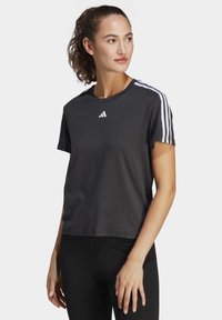 Tamsiai pilka sportinė marškinėliai su trumpomis rankovėmis, baltas Adidas logotipas ant krūtinės ir trys baltos juostelės ant kiekvienos peties. Minkšta audinio tekstūra.