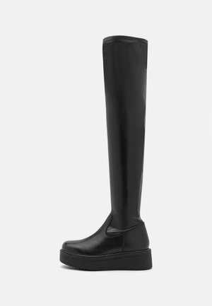 Bottes noires montantes au-dessus du genou en matière synthétique lisse, avec une semelle compensée et des panneaux latéraux élastiques pour un enfilage facile.