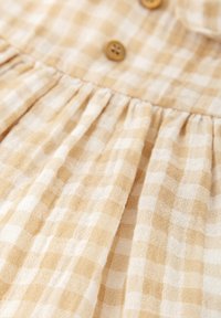 Tissu à carreaux vichy en beige et blanc avec des plis froncés et des boutons marron, créant un aspect texturé et léger.