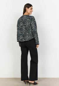 Black leopard print jacket with long sleeves, rounded neckline, and subtly textured fabric, paired with black wide-leg pants and heeled mules.