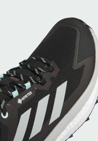 Chaussure de course noire avec un dessus en tissu texturé, design trois bandes blanches et logo GORE-TEX près des lacets. Semelle intermédiaire blanche pour un amorti.