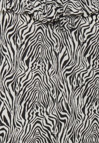 Tissu à imprimé zèbre noir et blanc présentant des lignes ondulées et une surface douce et texturée avec un bord froncé en haut.