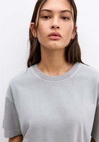 T-shirt en coton gris clair avec un col rond et des manches courtes ; texture lisse avec des détails de couture minimaux.