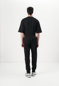 Black oversized T-shirt with short sleeves, paired with black elastic-waist pants. Sneakers feature a black and white design.