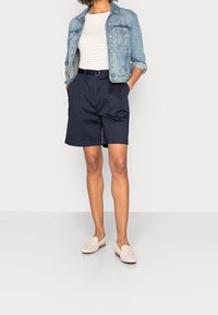 Kurtka dżinsowa na paskowanej bluzce, do tego granatowe szorty. Całość dopełniają beżowe mokasyny. Strój cechuje się luźnym krojem i casualowym stylem.