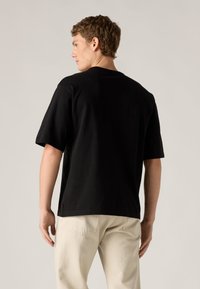 Μαύρο βαμβακερό μπλουζάκι με κοντά μανίκια, άνετη εφαρμογή και στρογγυλή λαιμόκοψη. Ορατή ραφή και μικρή ετικέτα λογοτύπου στο πλάι.