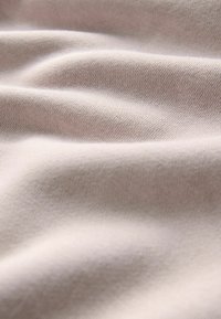 Tela de color beige claro con una textura suave, que presenta suaves ondulaciones y un patrón de tejido liso y uniforme. Adecuada para ropa o tapicería.