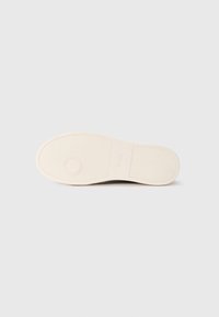 Hvit sneakersåle med teksturert gummimateriale, som har en sirkulær detalj og merkevarelogo. Glatt overflate og minimalistisk design.