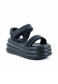 Czarne sandały na platformie z szerokimi paskami, wykonane z miękkiego materiału. Posiadają grubą, falistą podeszwę oraz regulowane zapięcie na rzep dla lepszego dopasowania.