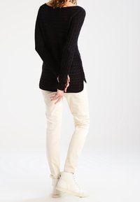 Svart kabelstickad tröja med långa ärmar, kombinerad med krämfärgade slim fit-byxor och vita hög-top sneakers. Slät textur, avslappnad passform.