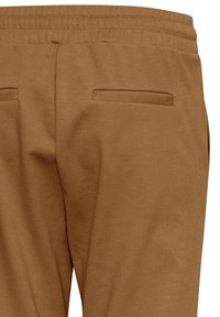 Brune, bløde stofbukser med elastisk talje, der har to flade baglommer og en glat overflade.