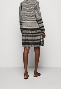 Gemustertes schwarz-weißes Kleid mit langen Ärmeln, unterschiedlichen geometrischen Designs und lockerem Schnitt. Es hat einen knielangen Saum und minimale Details.