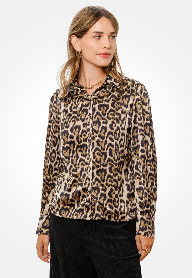 Bluzka w panterkę z miękkiego materiału, z kołnierzykiem, zapinana na guziki z przodu, z długimi rękawami. Uzupełniona złotymi dodatkami.