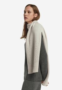 Jasnoszary sweter z dzianiny z długimi rękawami, ściągaczami przy mankietach i rozsianymi ozdobami. Noszony z ciemnoszarym body.