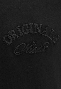 Crni pamučni dukserica s teksturiranim, izvezenim logotipom "ORIGINALS" i cursive detaljem "Studio". Glatka tkanina s jednostavnim dizajnom.