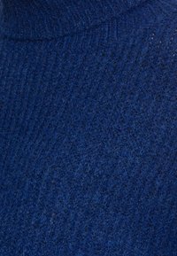 Stickad tröja i djupt blå, med ett strukturerat ribbmönster. Tyget verkar mjukt och tjockt, med en hög krage.