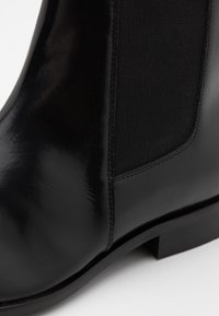 Černá kožená kotníková obuv s elastickými bočními panely, hladkou texturou, kulatou špičkou a nízkým blokovým podpatkem. Jemný šev na švech.