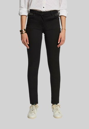 Jean skinny noir en denim, avec des accents cloutés sur les poches et un design classique à cinq poches, associés à des baskets blanches.