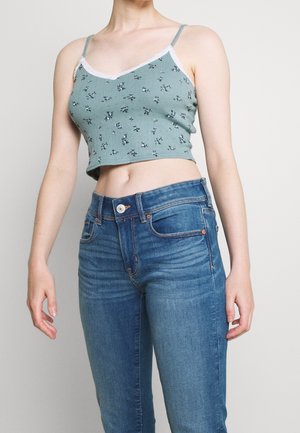 Turquoise cropped tanktop met bloemenpatroon en kanten randje, gecombineerd met blauwe denim high-waisted jeans met standaard zakken en een knoopsluiting.