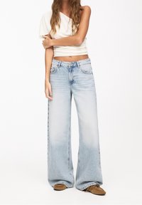 Světle modré džíny s širokými nohavicemi z měkkého denimu mají vybledlý vzhled, pas střední výšky, pět kapes a prošití. Kombinovány s přiléhavým topem.