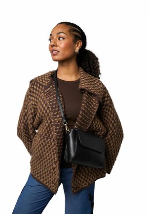 Hnedý a béžový pletený kardigán so vzorom a širokým golierom, nosený cez hnedý top, kombinovaný s modrými nohavicami a čiernou kabelkou cez rameno.