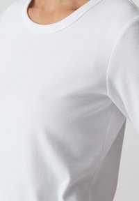 T-shirt bianco a coste con collo rotondo e texture morbida. Il tessuto ha una leggera lucentezza e una forma aderente.
