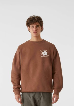 Brauner Sweatshirt mit runder Ausschnitt, versehen mit einem weißen Blumenmotiv und dem Text "VERLORENE JUGEND." Hergestellt aus weichem Stoff, lässige Passform.