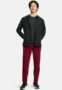 Chaqueta ligera negra con cremallera sobre una camiseta gris oscuro, combinada con pantalones deportivos burdeos y zapatillas negras con suelas blancas.