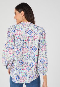 Blusa a maniche lunghe in tessuto leggero con un motivo geometrico colorato in tonalità di blu, rosa e verde. Vestibilità cadente con maniche arricciate.