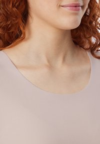 Helles rosa Oberteil mit einem breiten Rundhalsausschnitt, das weichen, elastischen Stoff und eine sanfte Textur an Hals und Schulter einer Person zeigt.