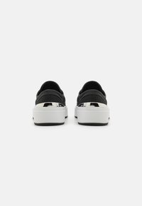 Sorte netting sneakers med en hvit plattformsåle, med metalliske detaljer ved hælen og en glatt tekstur på overdelen.