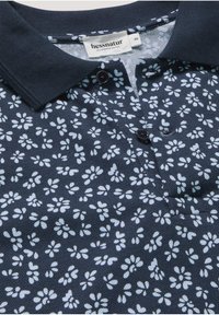 Polo bleu marine à imprimé floral blanc, boutons foncés et étiquette de la marque "hessnatur" près du col, taille 48.