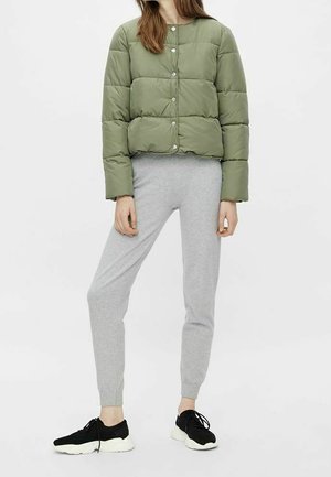 Oliivinvihreä toppatakki, jossa on lyhyt malli ja painonapit, yhdistettynä harmaisiin collegehousuihin ja mustiin urheilukenkiin.