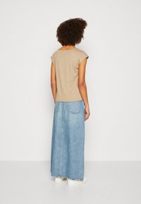 Top beige a maniche corte abbinato a una lunga gonna di jeans azzurro chiaro; texture morbida e design semplice con due tasche posteriori e taglio dritto.