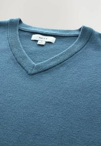 Niebieski sweter w serek, wykonany z miękkiej dzianiny. Posiada ribbrowany dekolt oraz metkę z nazwą marki. Gładka tekstura i średnia grubość.