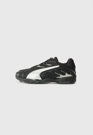 Zapatilla deportiva negra con diseños de llamas blancas y suela gruesa, mostrada en perfil lateral izquierdo sobre un fondo gris liso.