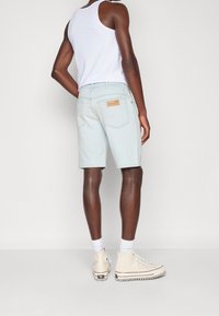 Světlé modré džíny šortky s kapsami vzadu, kožená značka na pase, nošeny s bílým tílkem a béžovými vysokými teniskami.