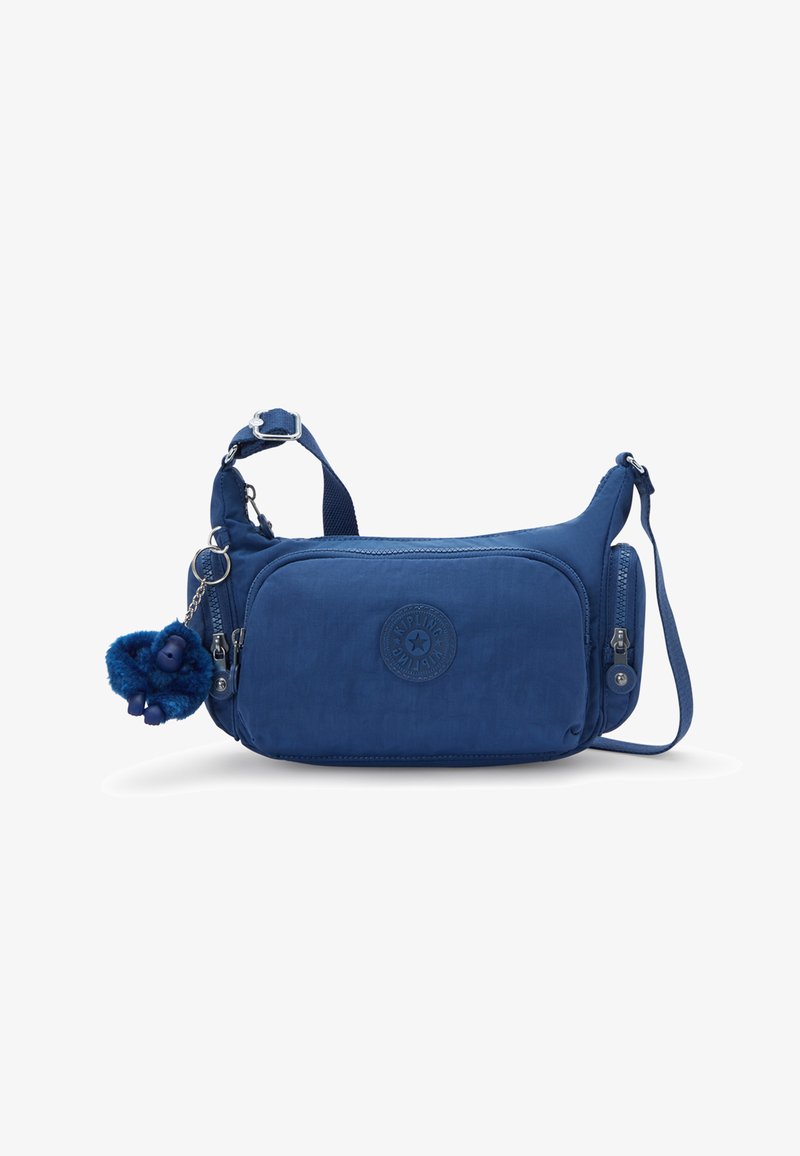Sac à bandoulière en nylon bleu de forme arrondie, avec une poche zippée à l'avant, un patch logo et un porte-clés singe en peluche. Sangle réglable incluse.