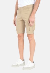 Pantaloni cargo khaki con due tasche laterali, in materiale di cotone, taglio dritto e chiusura con bottone frontale, indossati con sneakers bianche.