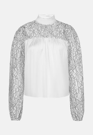 Blouse blanche avec de longues manches en dentelle noire transparente ornées de motifs floraux, un col haut, un buste texturé et une coupe décontractée.