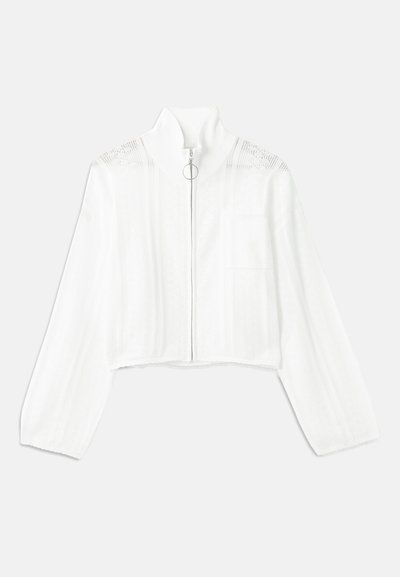 Pulover scurt alb tricotat, cu mâneci lungi, guler înalt, modele verticale texturate și fermoar frontal cu un mecanism circular pentru deschidere.