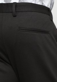 Pantalon noir à texture lisse, doté d'une poche arrière étroite et cachée ainsi que de passants pour ceinture, présentant un design sur mesure.