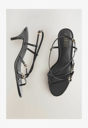 Schwarze Lackleder-Absatzsandalen mit dünnen Riemen, goldenen Hardware-Akzenten und minimalistischer Gestaltung. Hoher Absatz und offenes Zehen-Design.