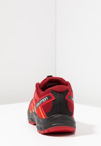 Red and black athletic shoes with a mesh upper, sturdy sole, and orange detailing. Features a cushioned interior and reinforced heel.