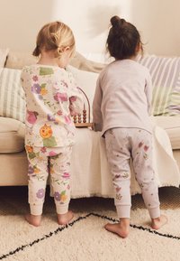 Deux enfants portent des pyjamas, l'un avec une base rose clair et des imprimés d'animaux colorés, l'autre en gris clair avec des motifs d'étoiles et de cœurs.