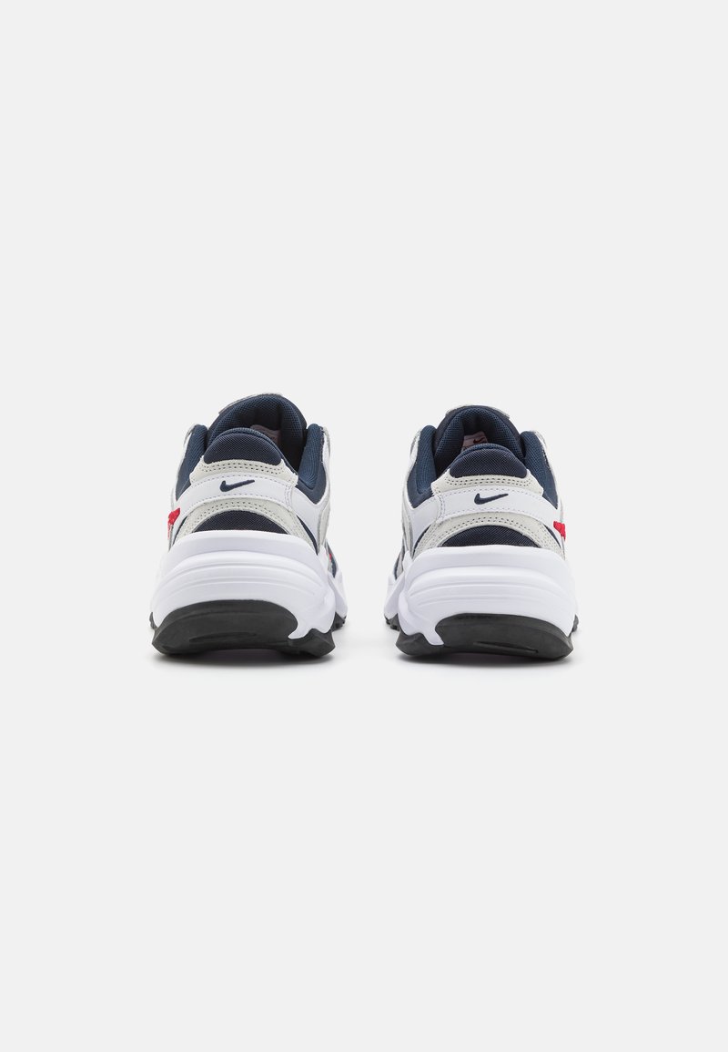 Zapatillas con un upper blanco y marino, material de malla y sintético, suela acolchada y un acento rojo cerca del talón. Vista trasera.