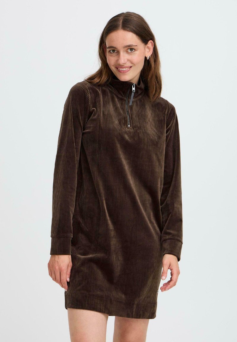 Robe en velours côtelé marron avec des manches longues, col zippé et texture nervurée ; design à mi-jarret et coupe décontractée, adaptée pour une tenue décontractée.