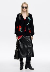 Czarny miękki kardigan z kolorowymi kwiatowymi wzorami, czerwony top, czarna skórzana spódnica i kozaki za kolano. Czarna torebka z metalowymi akcentami.