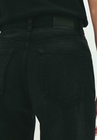 Schwarze Denim-Jeans mit hoher Taille, zwei hinteren Taschen mit schrägen Klappen und einem strukturierten Stoff mit matter Oberfläche.