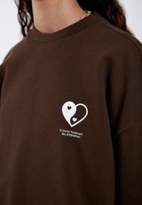 Felpa marrone con una grafica bianca di due cuori intrecciate sul petto, con un'etichetta del marchio sotto. Tessuto morbido.